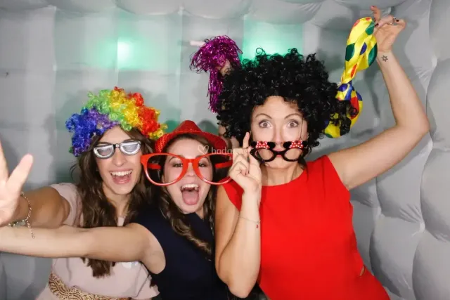 Tres invitadas con pelucas de colores y gafas de atrezzo gritando a la cámara