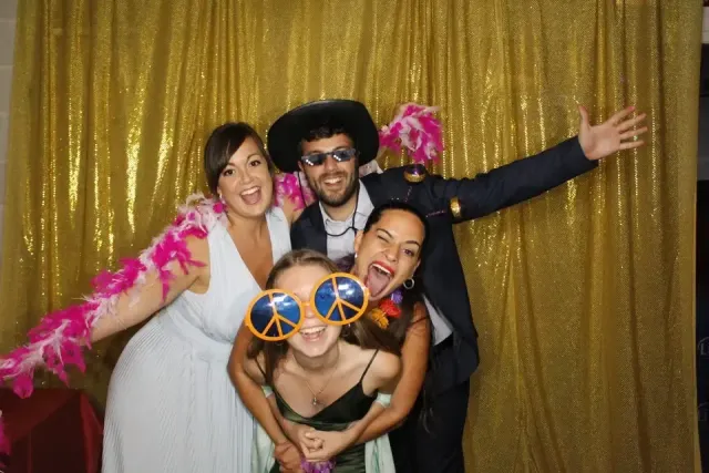 Invitados con boas de plumas y gafas gigantes ante una cortina dorada